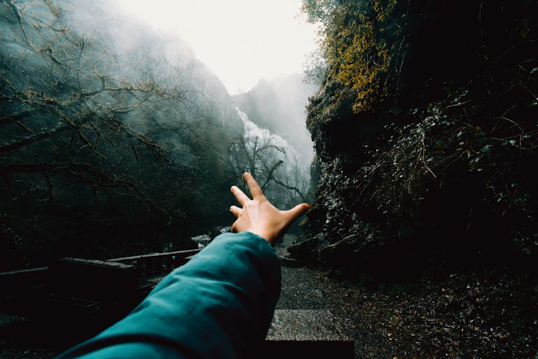 Are you stumbling in the dark? A person's hand reaches out towards a misty mountain trail surrounded by fog and trees.