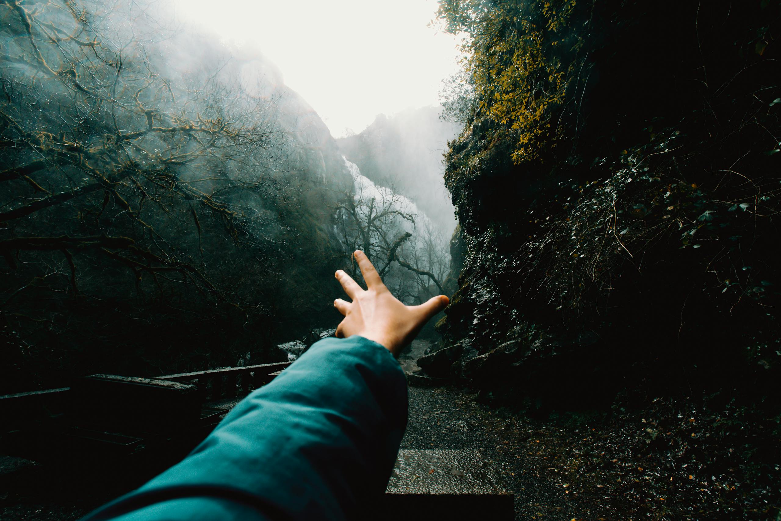 Are you stumbling in the dark? A person's hand reaches out towards a misty mountain trail surrounded by fog and trees.