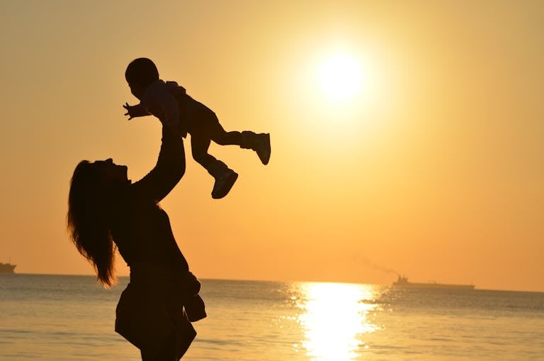 Celebrating mothers! Silhouette of a mother lifting her child at a sunset beach, capturing warmth and love.
